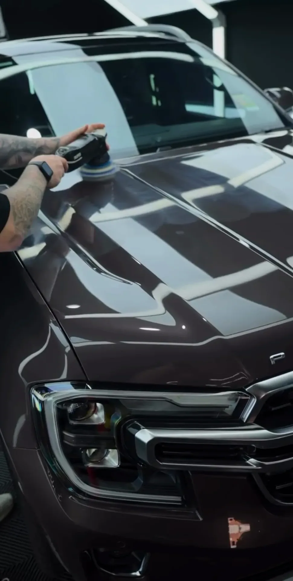 Machine polishing the bonnet of a dark SUV